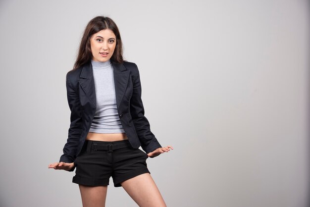 Joven empresaria en chaqueta de pie y posando sobre una pared gris.