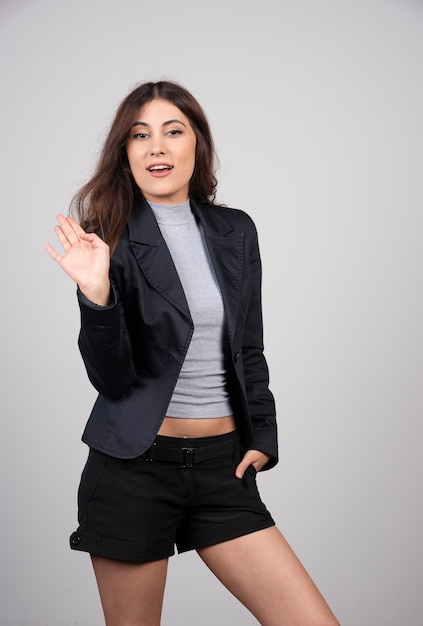 Joven empresaria en chaqueta de pie y posando sobre una pared gris.