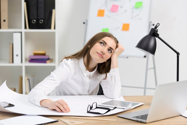 Joven empresaria contemplada con papel blanco; Anteojos y tableta digital en escritorio de madera.