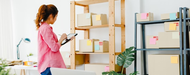 Joven empresaria empresaria de Asia comprueba la orden de compra del producto en stock y ahorra en el trabajo de la tableta en la oficina en casa Propietario de una pequeña empresa, entrega de mercado en línea, concepto independiente de estilo de vida.