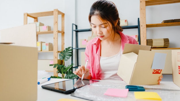 Joven empresaria empresaria de Asia comprueba la orden de compra del producto en stock y ahorra en el trabajo de la tableta en la oficina en casa Propietario de una pequeña empresa, entrega de mercado en línea, concepto independiente de estilo de vida.