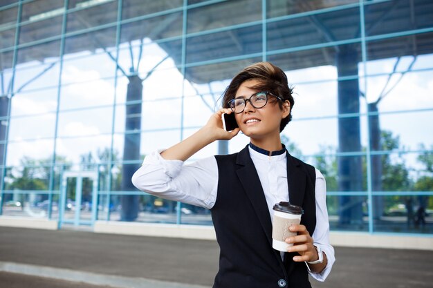 Joven empresaria exitosa hablando por teléfono, de pie cerca del centro de negocios.