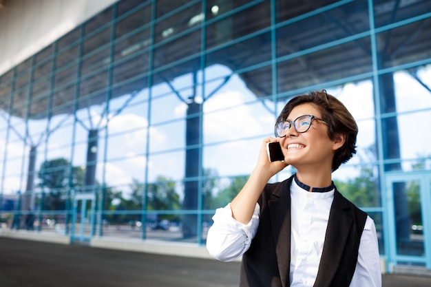 Joven empresaria exitosa hablando por teléfono, de pie cerca del centro de negocios.