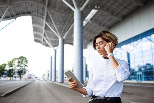 Joven empresaria exitosa hablando por teléfono, de pie cerca del centro de negocios.