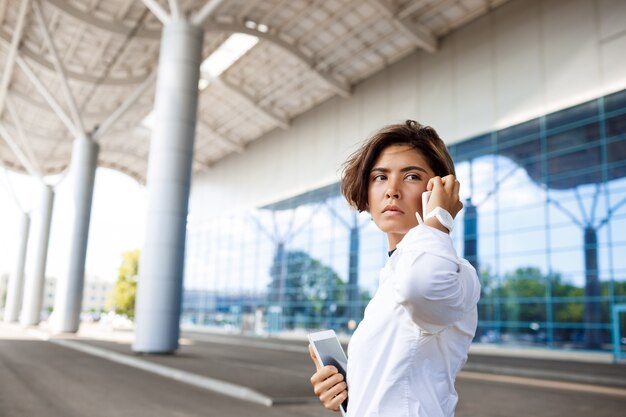 Joven empresaria exitosa hablando por teléfono, de pie cerca del centro de negocios.