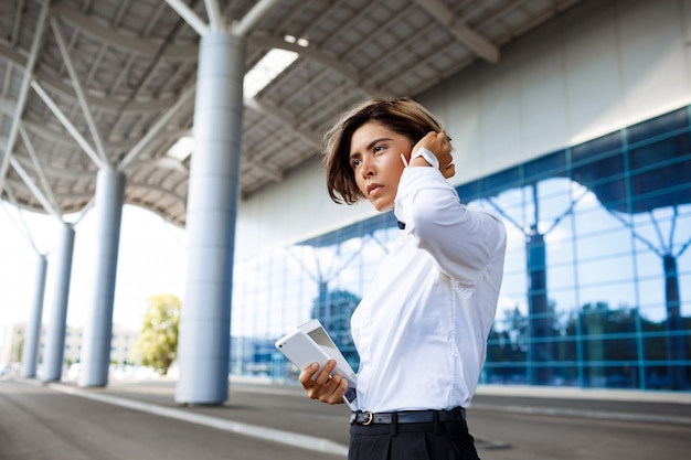 Joven empresaria exitosa hablando por teléfono, de pie cerca del centro de negocios.