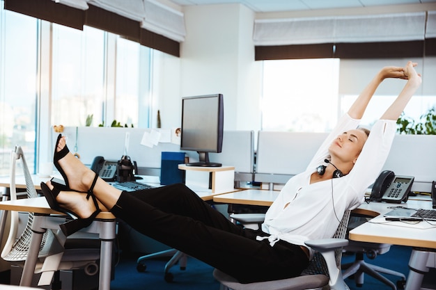 Joven empresaria exitosa hermosa descansando, relajándose en el lugar de trabajo, oficina