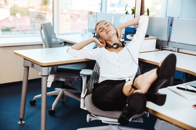 Joven empresaria exitosa hermosa descansando, relajándose en el lugar de trabajo, oficina