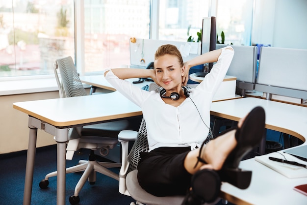 Joven empresaria exitosa hermosa descansando, relajándose en el lugar de trabajo, oficina