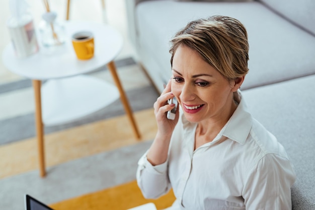 Joven empresaria feliz trabajando en casa y comunicándose por teléfono celular