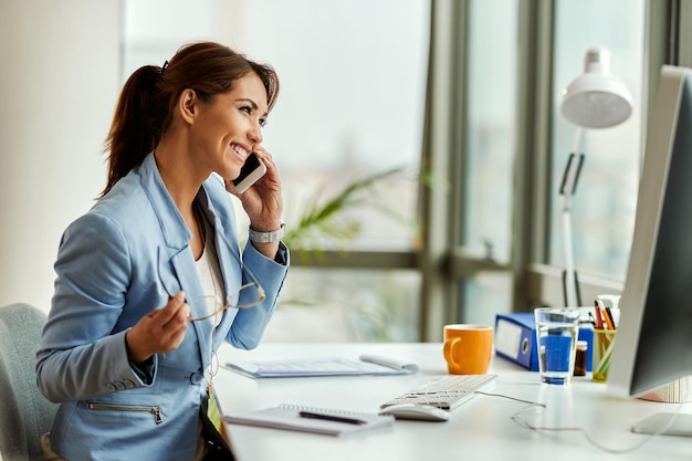 Joven empresaria feliz usando teléfono celular y haciendo una llamada telefónica en la oficina