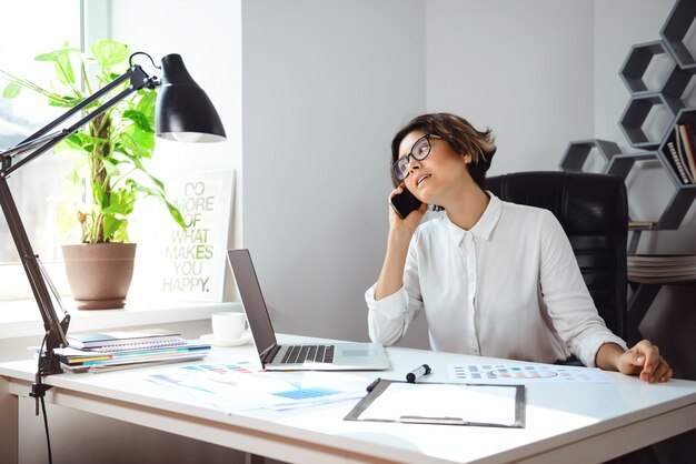 Joven empresaria hermosa hablando por teléfono en el lugar de trabajo en la oficina.