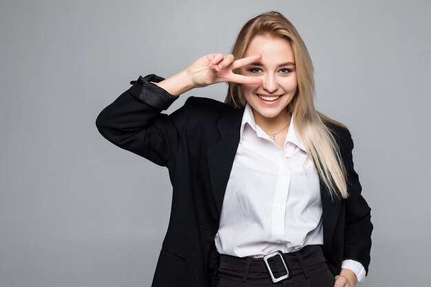 Joven empresaria hermosa haciendo el símbolo de paz con los dedos sobre la cara, sonriendo alegre mostrando victoria de pie sobre la pared blanca aislada