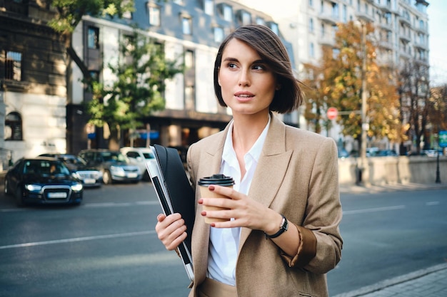 Joven empresaria hermosa con laptop y café para ir a la calle de la ciudad