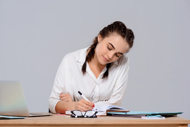 Joven empresaria hermosa sentada en el lugar de trabajo, escribiendo sobre la pared púrpura