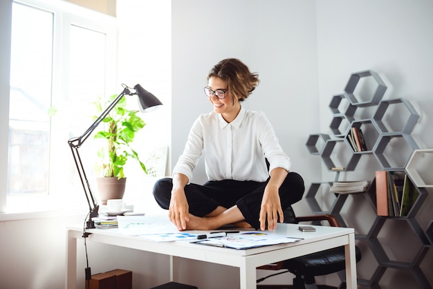 Foto gratuita joven empresaria hermosa sentada en la mesa en el lugar de trabajo en la oficina.