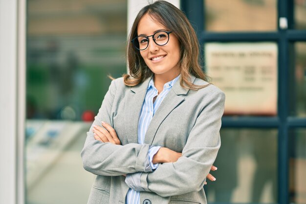 Joven empresaria hispana con los brazos cruzados sonriendo feliz en la ciudad.