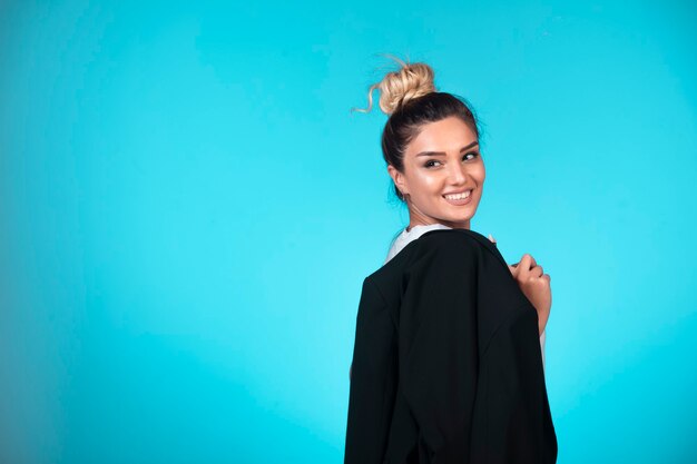 Joven empresaria con moño sosteniendo una chaqueta negra y sonriendo.