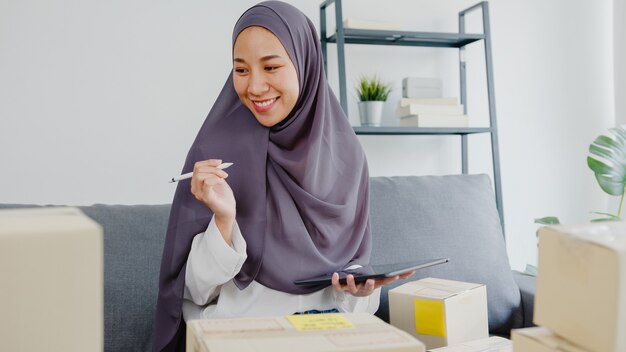 Joven empresaria musulmana verifique la orden de compra del producto en stock y guarde para el trabajo de la tableta en la oficina en casa.