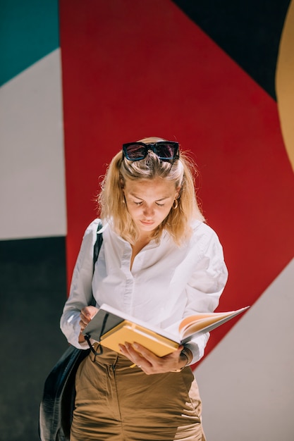 Joven empresaria de pie contra la pared de color leyendo el libro