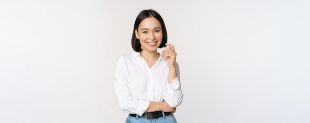 Joven empresaria profesional asiática de pie en ropa de oficina sonriendo y con un fondo blanco confiado