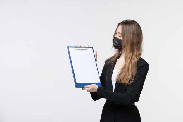 Joven empresaria soñadora en traje con su máscara médica y mostrando documentos en la pared blanca