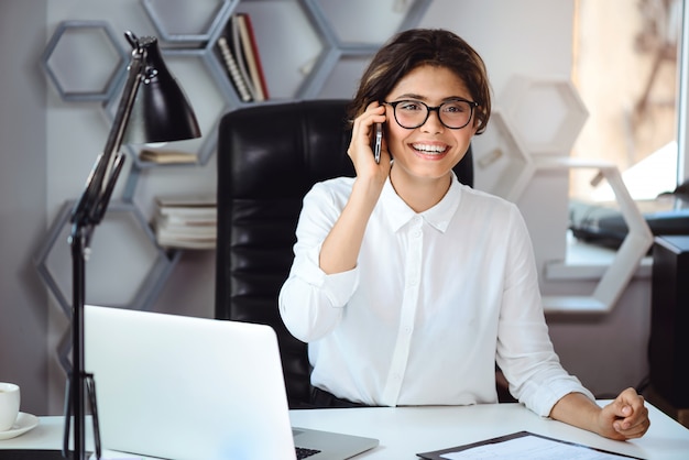 Joven empresaria sonriente hermosa hablando por teléfono en el lugar de trabajo en la oficina.