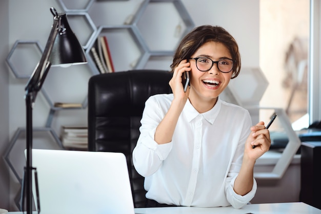 Joven empresaria sonriente hermosa hablando por teléfono en el lugar de trabajo en la oficina.