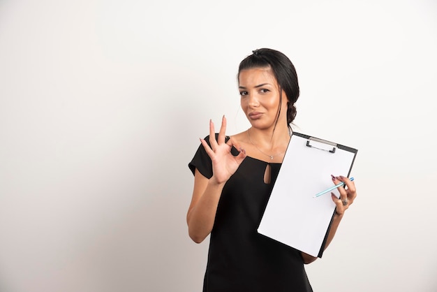 Joven empresaria sosteniendo documentos y haciendo el signo ok.