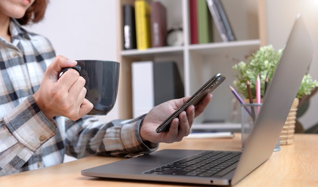 Joven empresaria sosteniendo una taza de café y usando un teléfono inteligente para la tecnología de mensajes sms y el concepto de red de medios sociales.