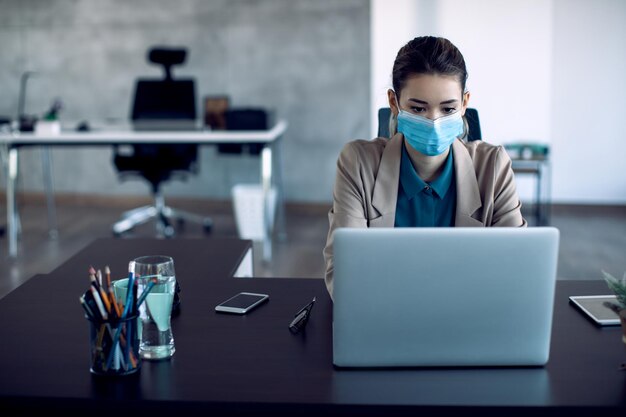 Joven empresaria trabajando en una computadora en la oficina durante la pandemia del coronavirus