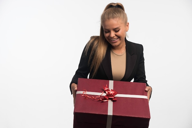 Joven empresaria en traje negro sosteniendo una caja de regalo grande y sonriendo.