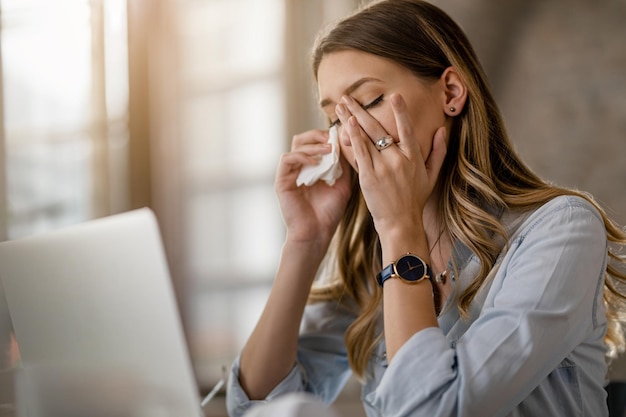 Joven empresaria con virus del resfriado y la gripe que tiene dolor de cabeza mientras trabaja en la oficina