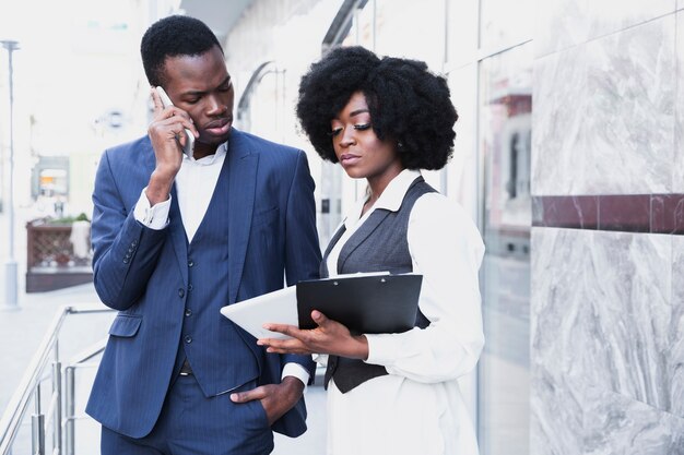 Un joven empresario africano hablando por teléfono móvil mirando a su tableta digital por su colega