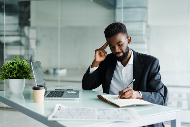 Joven empresario africano trabajando en la oficina en la computadora portátil y hacer un aviso en el cuaderno