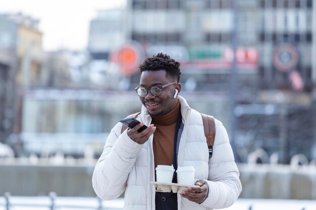Joven empresario afroamericano sosteniendo café en una taza de cartón y hablando por teléfono