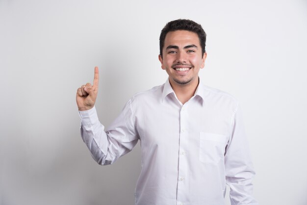 Joven empresario apuntando al revés sobre fondo blanco.