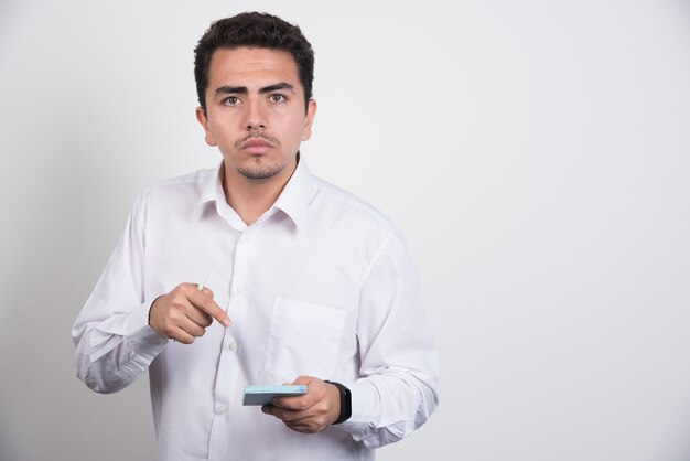 Joven empresario apuntando a blocs de notas sobre fondo blanco.