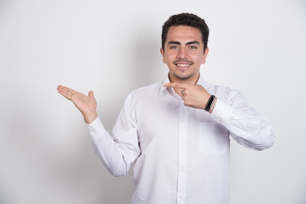 Joven empresario apuntando a su lado sobre fondo blanco.