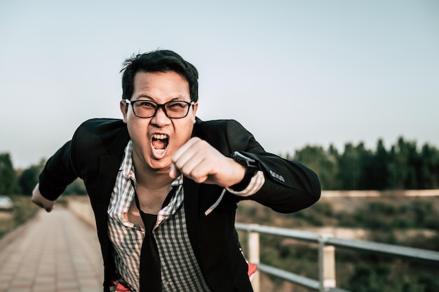 Foto gratuita joven empresario asiático divertido con camisa y corbata con pantalones cortos y anteojos en un espacio de copia de postura de manera loca y divertida