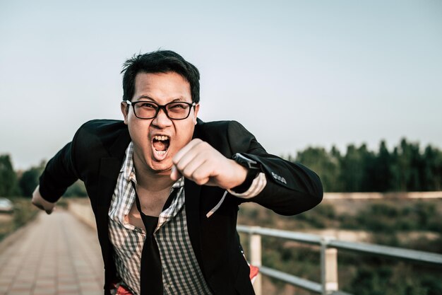 Joven empresario asiático divertido con camisa y corbata con pantalones cortos y anteojos en un espacio de copia de postura de manera loca y divertida