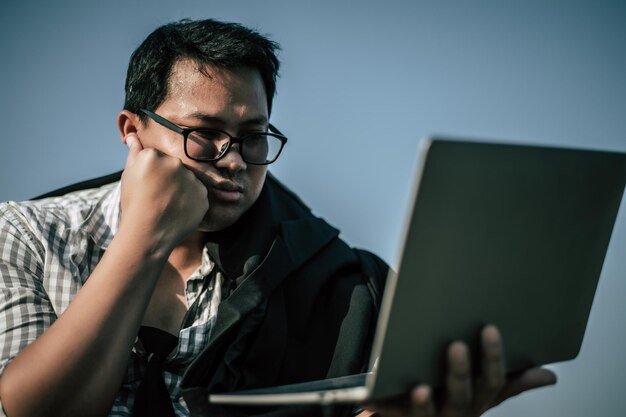 Joven empresario asiático con laptop con camisa y corbata con pantalones cortos y anteojos con problemas y estrés o decepción del trabajo en el espacio exterior de la oficina corporativa