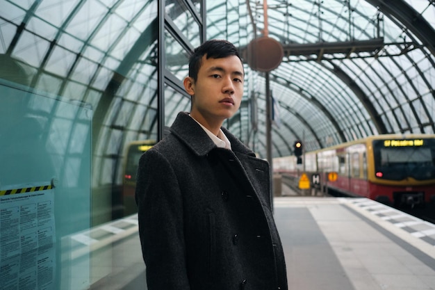 Joven empresario asiático serio con abrigo esperando el tren en la estación de metro de la ciudad