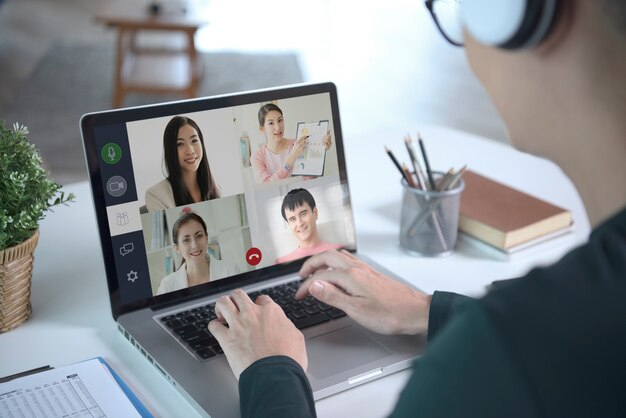 Joven empresario asiático usa auriculares trabajando de forma remota desde casa y reunión de videoconferencia virtual con colegas empresarios. distanciamiento social en el concepto de oficina en casa.