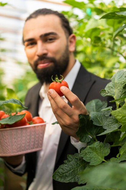 Joven empresario barbudo sosteniendo tomate y mirando a la cámara