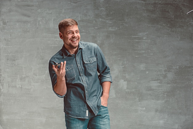 Foto gratuita el joven empresario caucásico sonriente en gris con teléfono