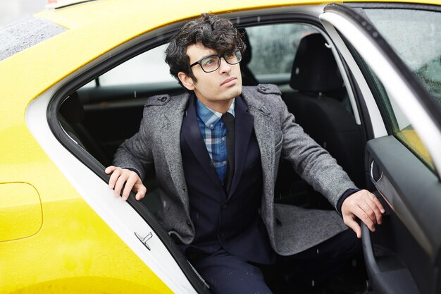 Joven empresario dejando taxi bajo la lluvia