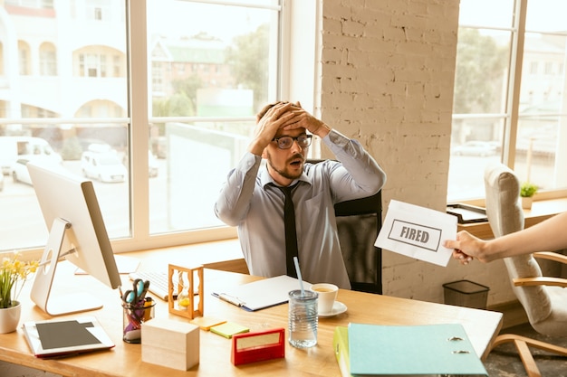 Joven empresario despedido, parece molesto. Tiene que empacar sus pertenencias de oficina y dejar el lugar de trabajo para un nuevo trabajador. Problemas en la ocupación, estrés, desempleo, nueva forma de vida o fin de carrera.