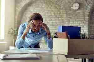 Foto gratuita joven empresario disgustado con dolor de cabeza después de ser despedido de su trabajo en la oficina