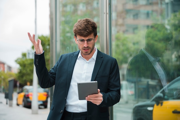 Joven empresario encogiéndose mientras mira a la tableta digital